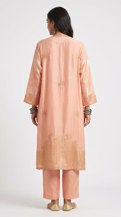 Woman wearing a peach kurta with gold embroidery on a white background