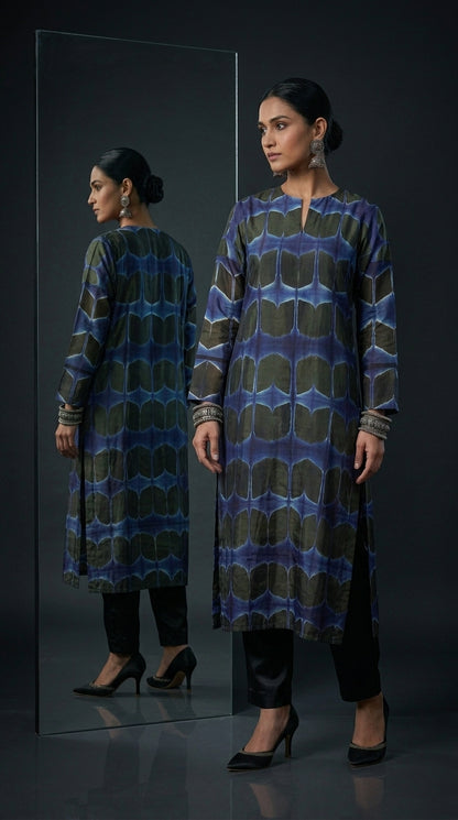 Woman wearing a patterned blue and black kurta standing in front of a mirror on a black background