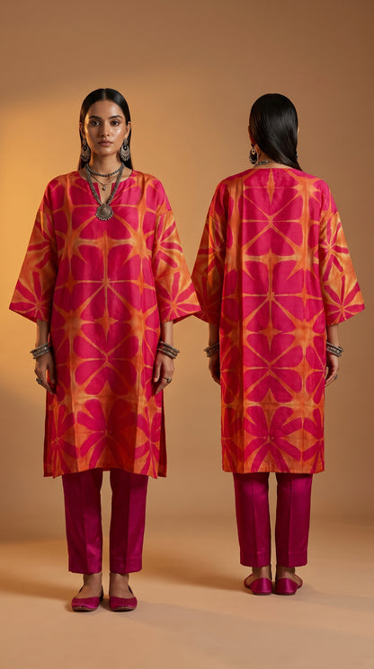 Woman wearing a pink and orange patterned kurta with magenta pants, standing against a beige background.