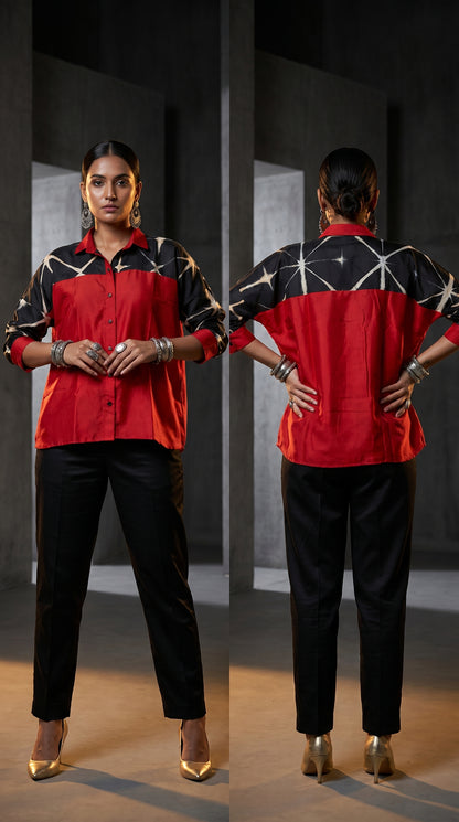 Woman wearing a red and black patterned shirt with black pants, standing in front of a mirror.