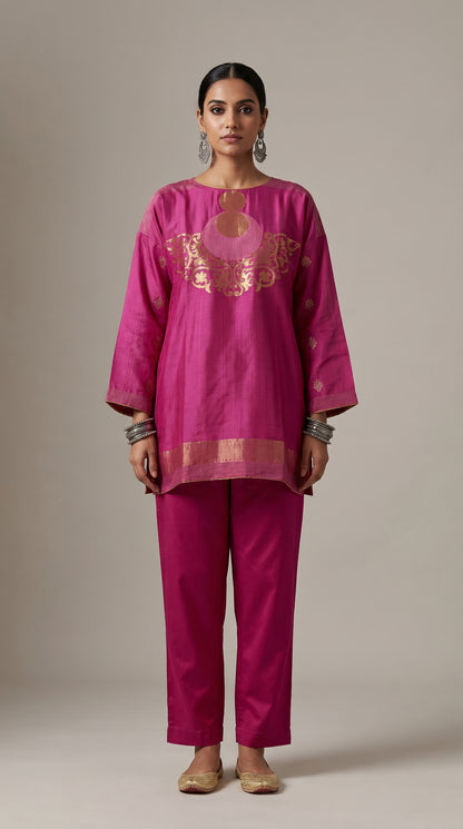 Woman wearing a magenta traditional outfit with gold embroidery on a beige background
