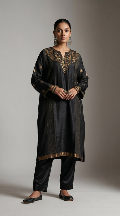Woman wearing a black traditional kurta with gold embroidery on a gray background