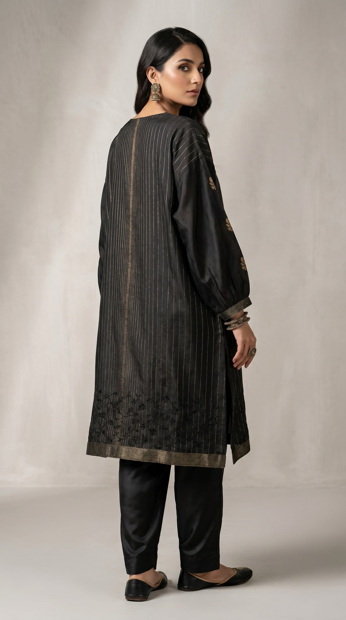 Woman wearing a black traditional kurta with embroidery on a plain background