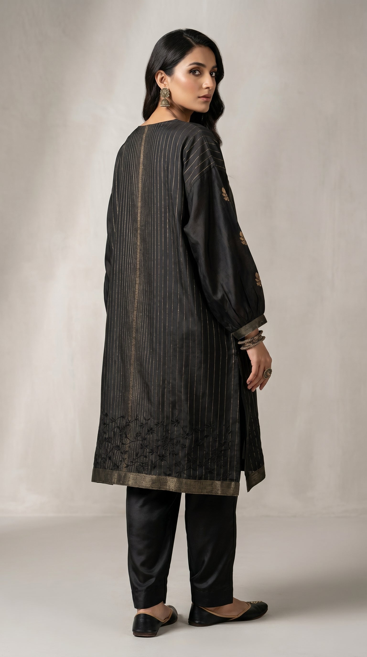Woman wearing a black traditional kurta with embroidery on a plain background
