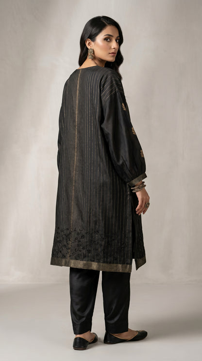 Woman wearing a black traditional kurta with embroidery on a plain background