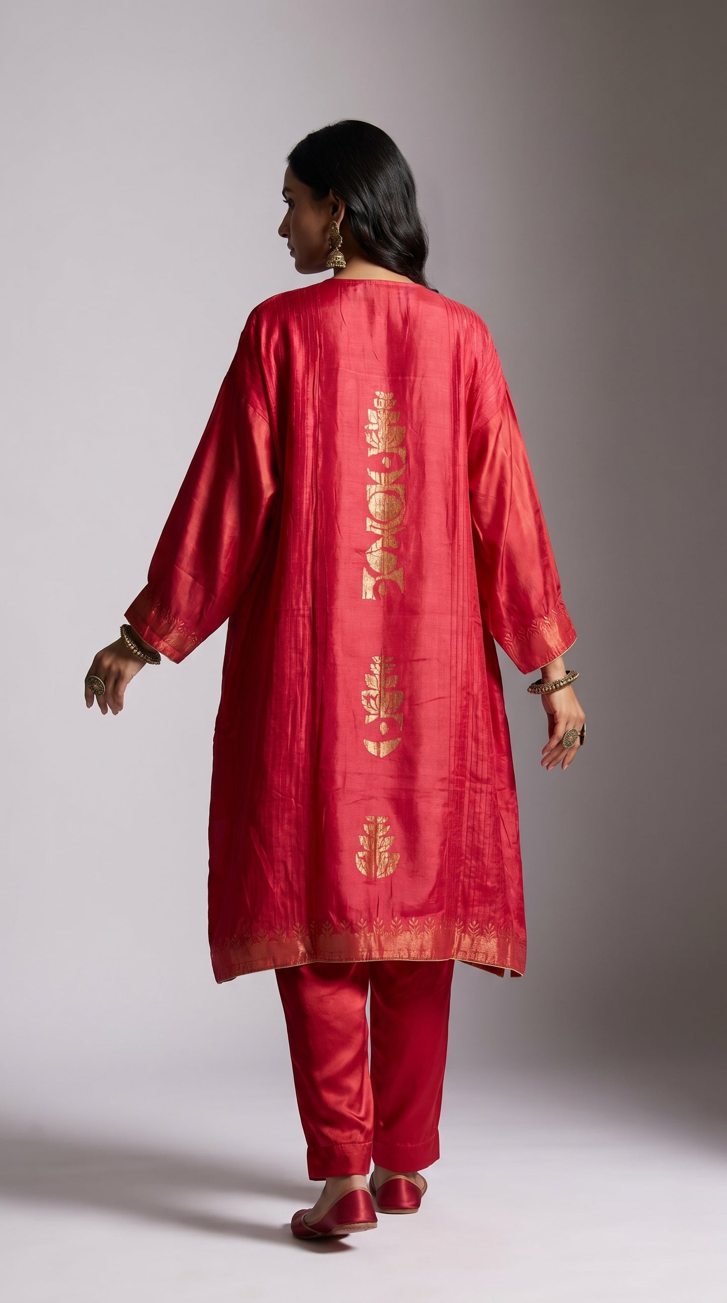 Person wearing a pink traditional kurta with gold embroidery on a plain background
