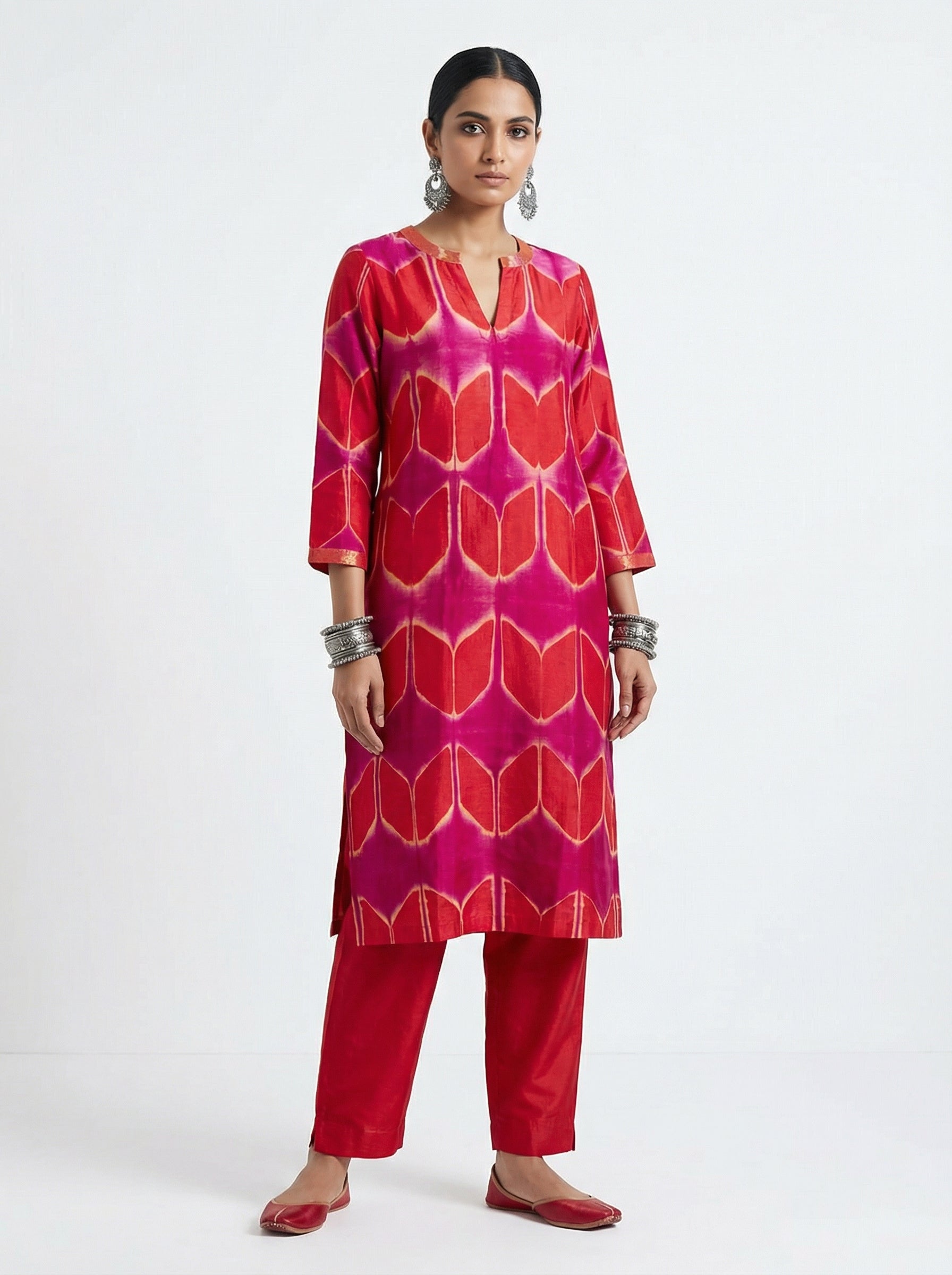 Woman wearing a red and pink patterned kurta with pants on a white background